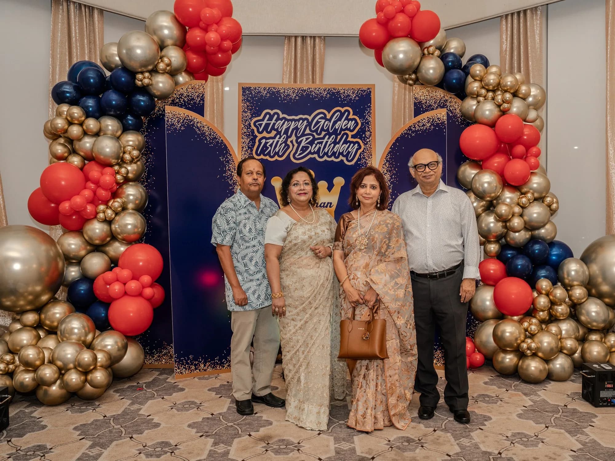Family portrait at a red, gold and navy balloon arch