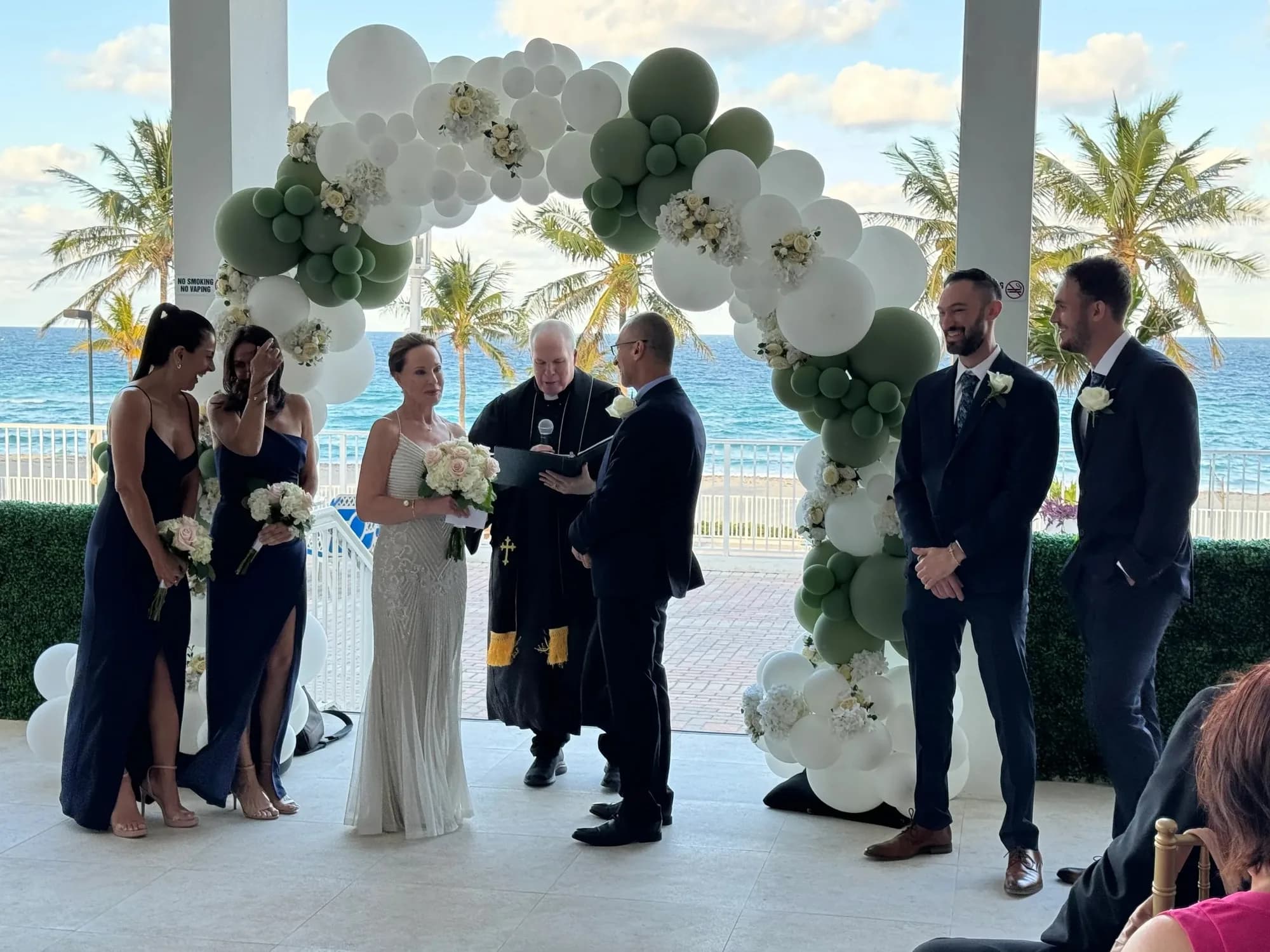 Beachfront wedding ceremony with a white and sage balloon arch