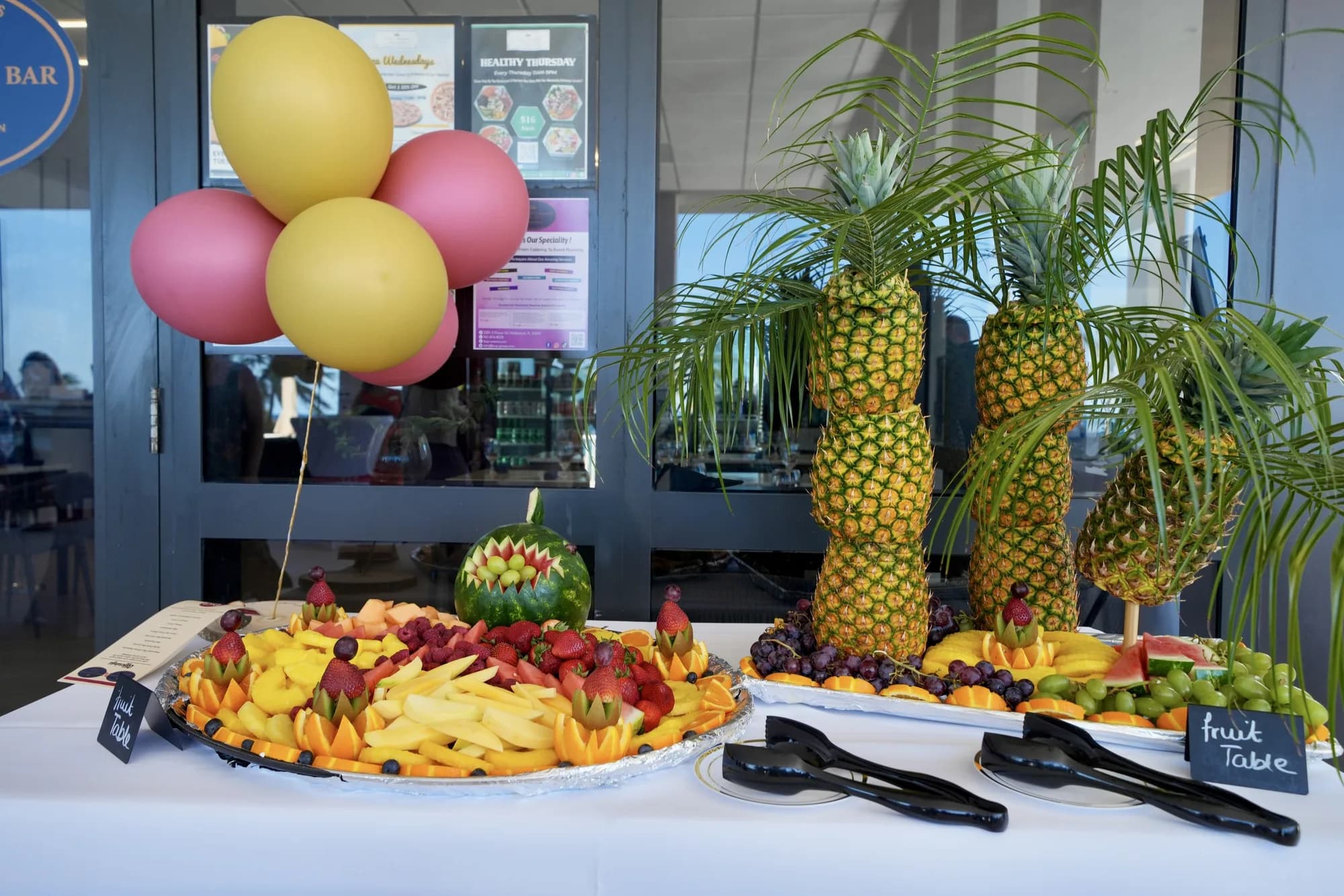 Tropical fruit display with a carved pineapple centerpiece and balloons at a catered party